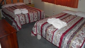 Two single beds with floral bedding, a bedside table with a lamp, and a window with orange curtains. - 1470 Murietta Drive (South Lake Tahoe)