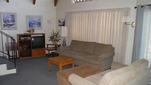 A living room with a sofa, a coffee table, a TV, and a staircase. - 1470 Murietta Drive (South Lake Tahoe)