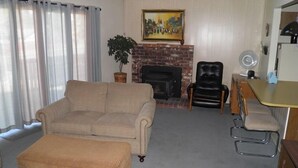 A living room with a beige sofa, a matching ottoman, a black leather chair, a small table with a chair, and a fireplace with a painting above it. - 1470 Murietta Drive (South Lake Tahoe)