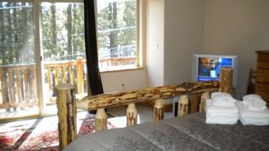 Un dormitorio con cama, televisión, banca de madera y balcón con vista a árboles.