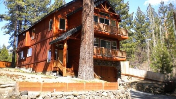 Una cabaña de troncos de dos pisos con un balcón en el nivel superior, rodeada de árboles.