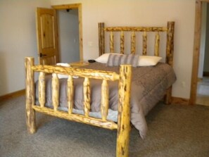 A single bed with a wooden frame and a gray mattress in a room with a carpeted floor and a wooden door.