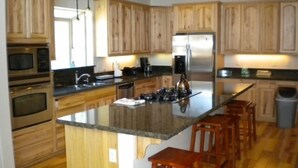 Una cocina moderna con armarios de madera, electrodomésticos de acero inoxidable, una isla central con taburetes y un amplio ventanal que proporciona luz natural.
