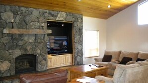 Una sala de estar con chimenea de piedra, un sillón de cuero, una mesa de centro de madera y un sofá color beige.