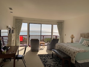 A room with a bed, a desk, a chair, and a sofa. There is a large window with a view of the ocean. - Arky's B&B (Smith River)