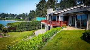 A modern house with a deck overlooking a body of water, surrounded by lush greenery. - Arky's B&B (Smith River)