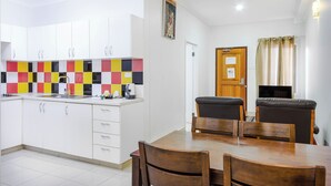 A modern kitchen with white cabinets, a colorful backsplash, and a dining area with wooden chairs and a table. - Citi Serviced Apartments - Korobosea (Port Moresby)