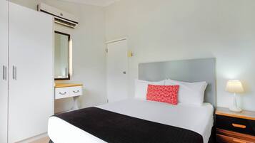 Una camera d'albergo con un letto, un comodino con una lampada, un armadio e uno specchio.
