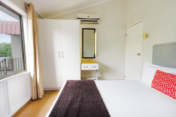 A bedroom with a bed, a wardrobe, a mirror, and a window with curtains.