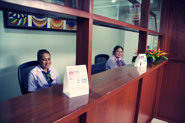 A reception desk with a sign, a computer, and a plant.