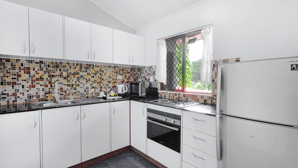 A modern kitchen with white cabinets, a tiled backsplash, and a window with a view of greenery. - Citi Serviced Apartments - Korobosea (Port Moresby)