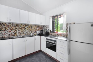 A modern kitchen with white cabinets, a tiled backsplash, and a window with a view of greenery. - Citi Serviced Apartments - Korobosea (Port Moresby)