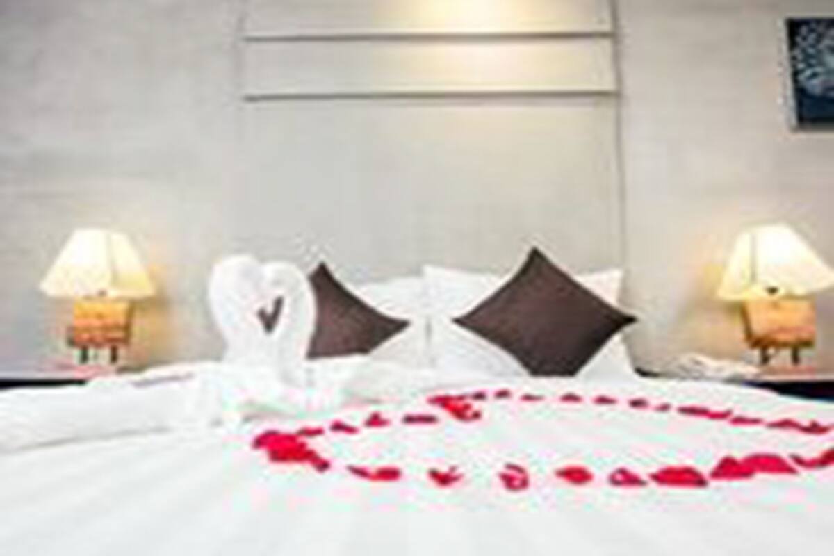 Una cama bien hecha con sábanas blancas y una decoración de pétalos de rosa en forma de corazón.