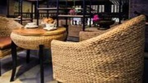 Een gezellige zithoek met rieten stoelen en een ronde tafel, met een boekenplank en decoratieve objecten op de achtergrond.