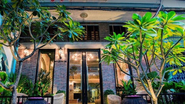 Een boetiekhotel met een gevel van baksteen, grote glazen deuren en terras met potplanten.