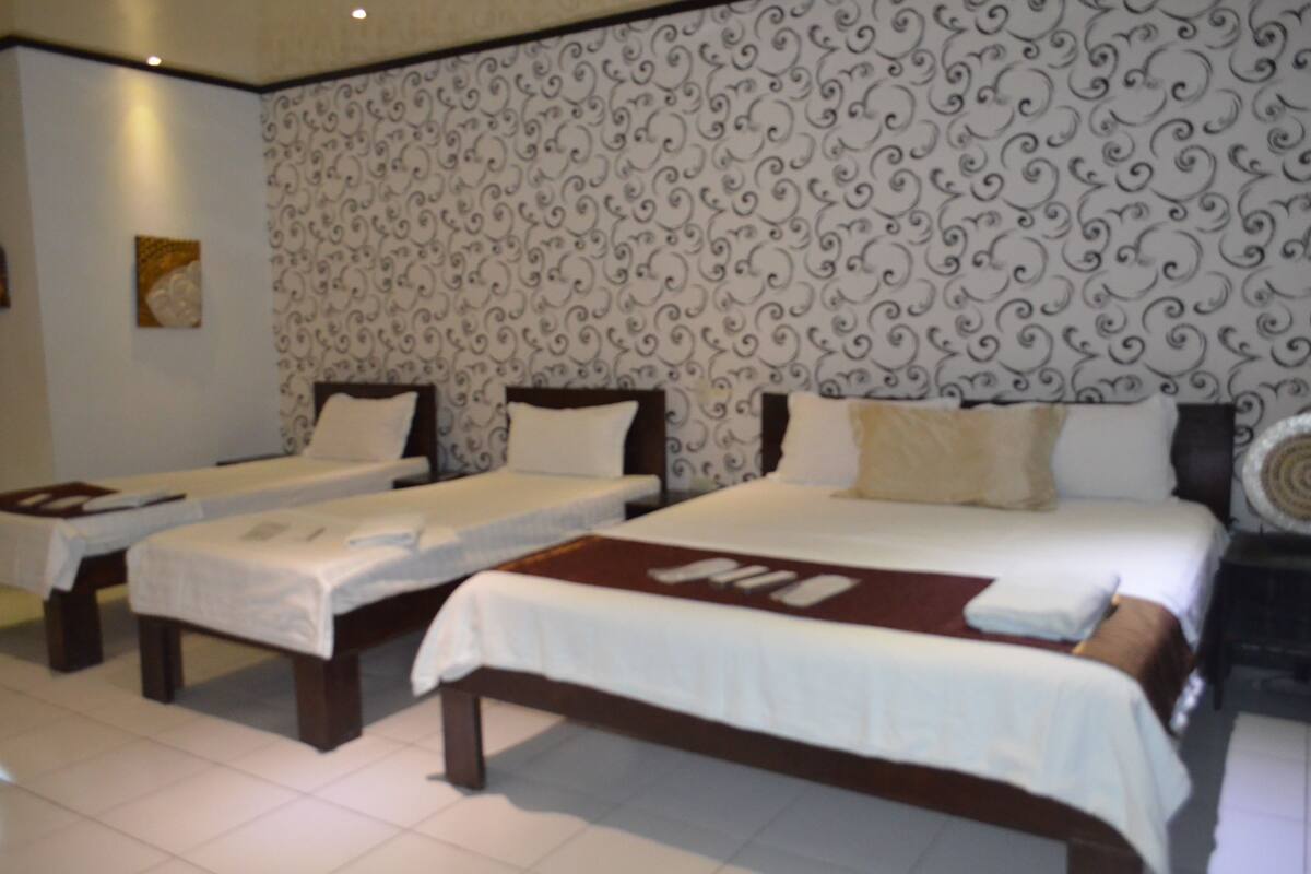 A hotel room with two single beds and one double bed, all with white linens.