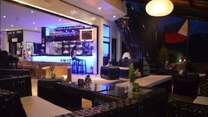 Zona de bar con taburetes y barra, una escalera y asientos con cojines.