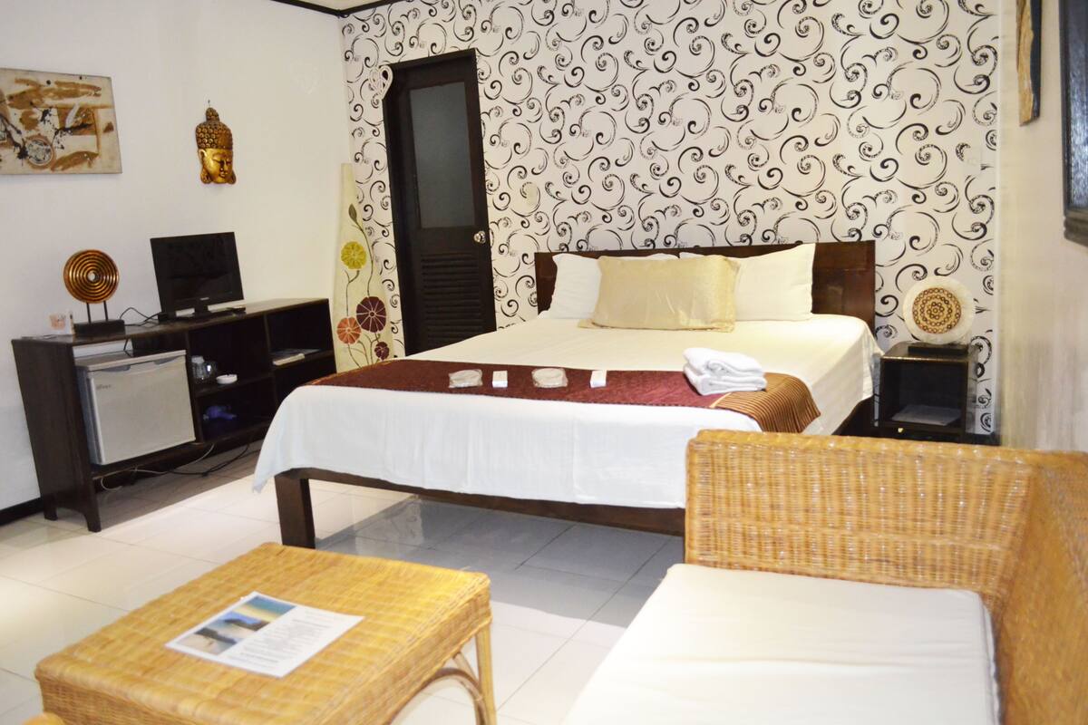 A hotel room with a bed, a television, a desk, and a wicker chair.