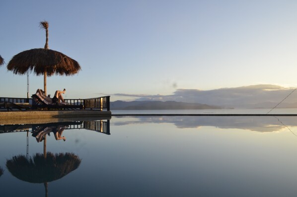 A serene pool area with a clear view of distant mountains, a thatched umbrella, and a wooden deck.