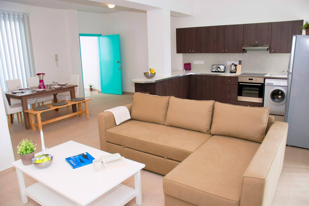 Un soggiorno moderno con un divano modulare beige, un tavolino da caffè bianco e un'area pranzo con tavolo e sedie in legno.