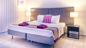 Un hotel moderno con una cama grande, dos mesitas de noche con lámparas y vistas a la ciudad.