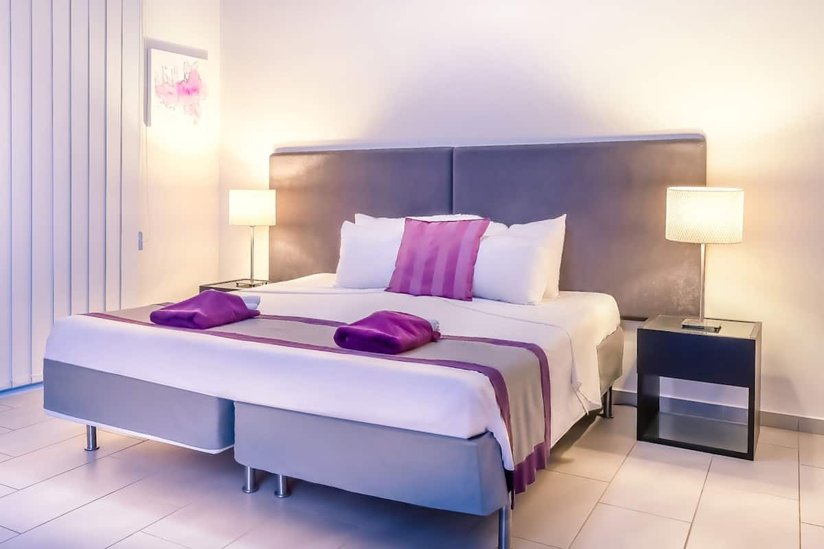 Una camera d'albergo moderna con un letto grande, due comodini con lampade e vista sulla città.
