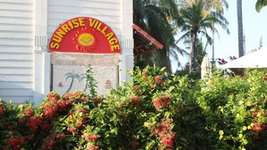 Ein Gebäude mit einem Schild, auf dem 'Sunrise Village' steht, und einer Palme im Hintergrund.