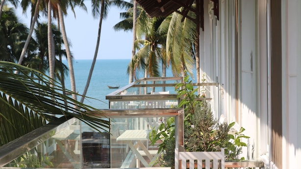 Ein Balkon mit Glasveranda, Palmen und Blick aufs Meer.