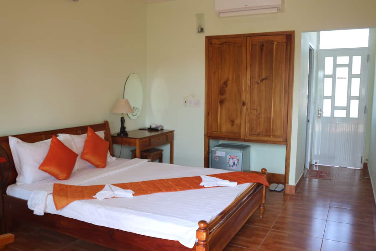 Ein Hotelzimmer mit einem hölzernen Bett, einem Schreibtisch mit Lampe, einem Kleiderschrank und einem kleinen Kühlschrank.