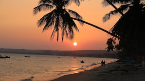 Eine Strandlandschaft bei Sonnenuntergang, mit Palmen und Booten auf dem Wasser.