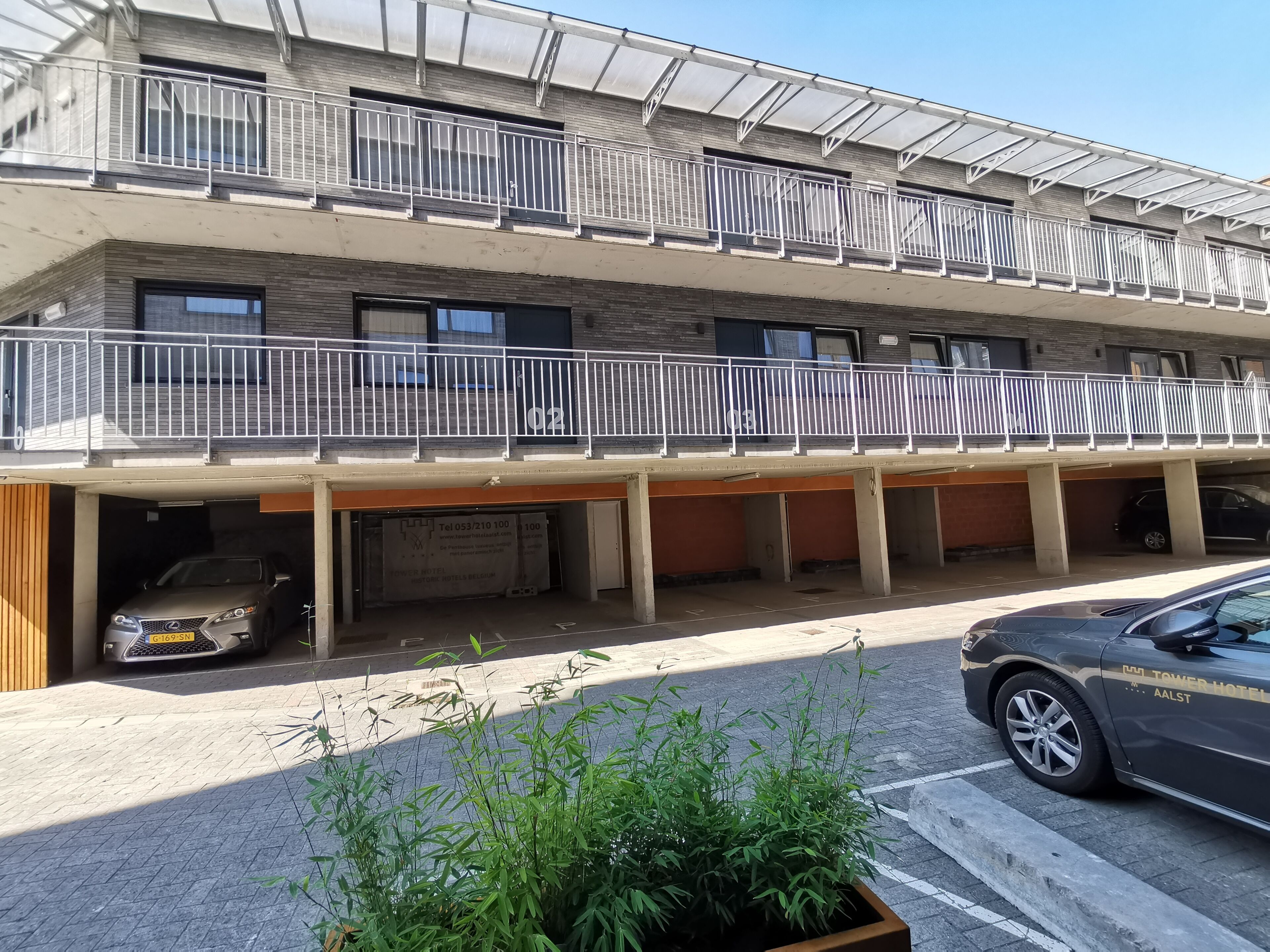 A multi-story hotel with a covered parking area, a staircase, and a balcony with railings.