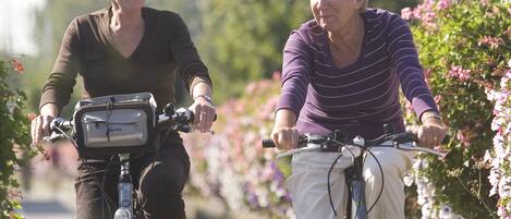 Two people riding bicycles on a paved path surrounded by greenery and flowers.
