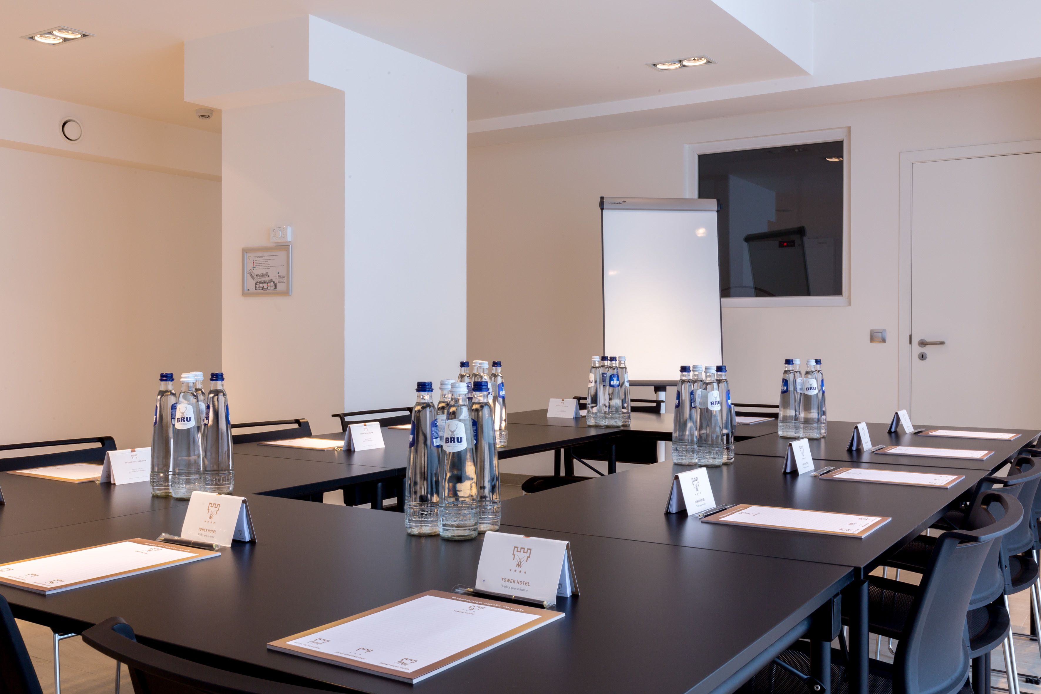 Une salle de conférence avec une longue table, des chaises, des bouteilles d’eau, des plaques nominatives et un tableau blanc.