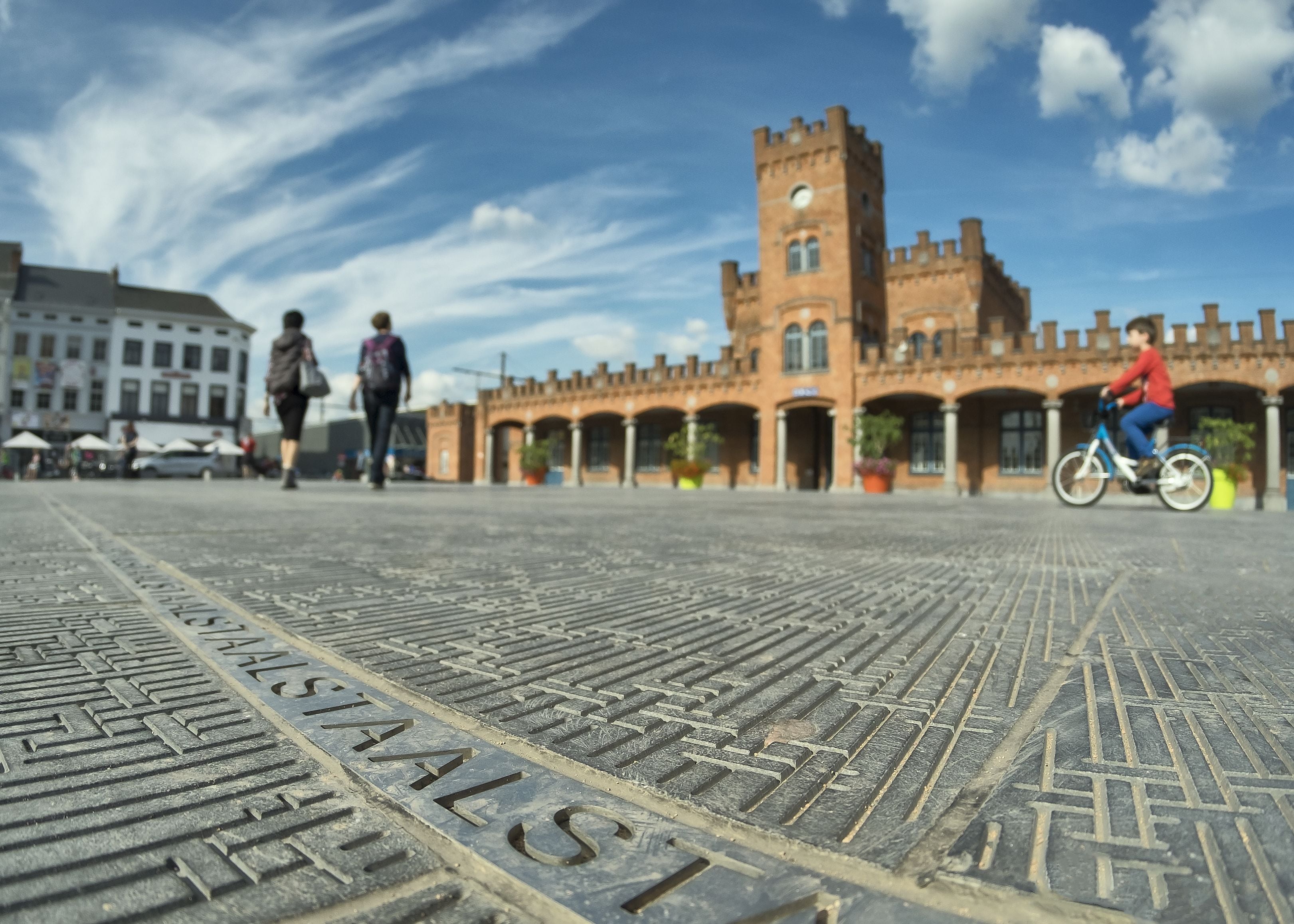 A cobblestone plaza with a historic building featuring a tower and arches in the background.
