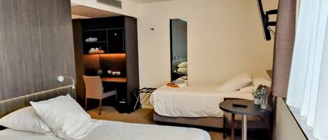 A hotel room with two beds, a desk, a chair, a small table, and a TV.