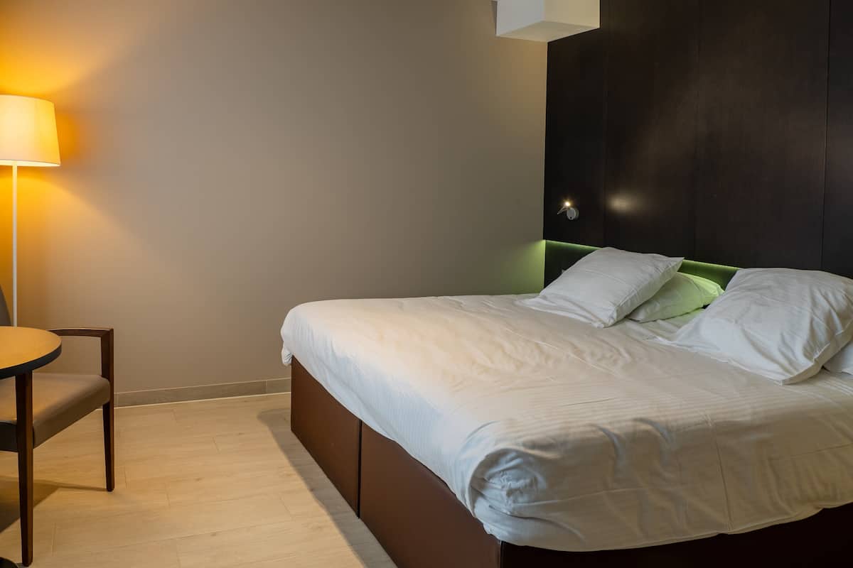 Una cama bien tendida con sábanas blancas, cabecera verde y una lámpara de noche.