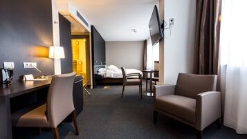 Una camera d'albergo con un letto, una scrivania con lampada, una sedia e una TV a muro.