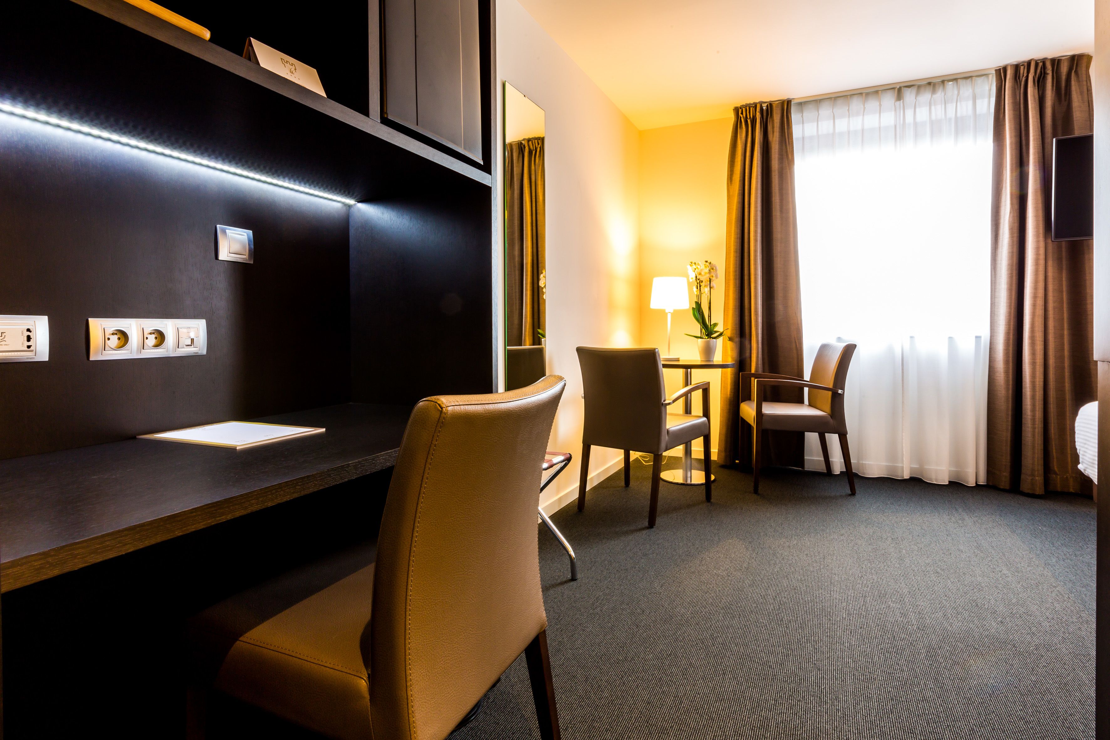 Een hotelkamer met een bureau, twee stoelen, een lamp en een televisie.