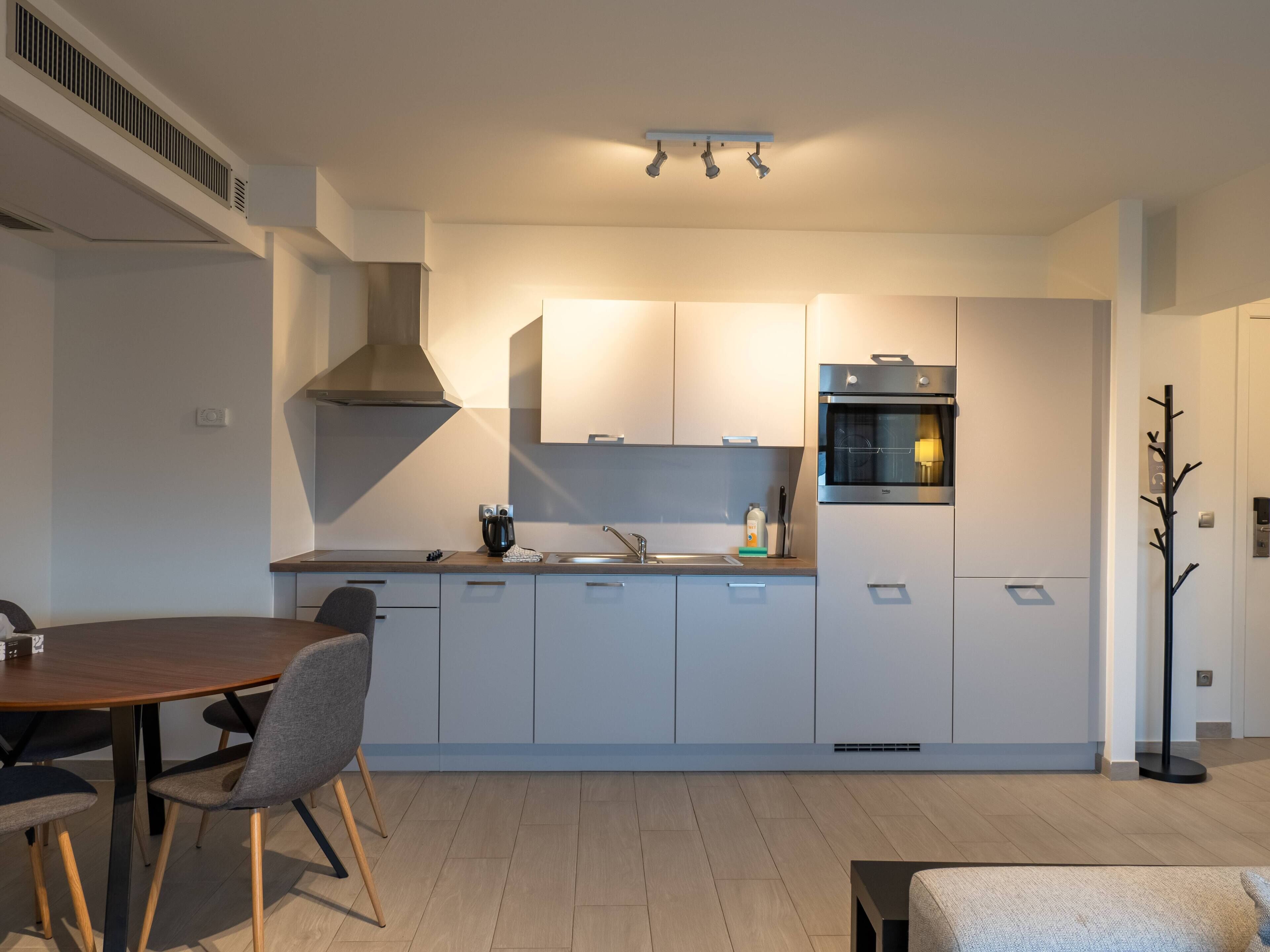 Eine moderne Küche mit weißen Schränken, einem eingebauten Ofen und einem Essbereich mit einem Holztisch und Stühlen.