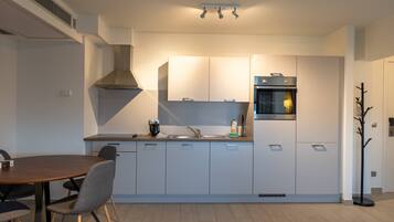 A modern kitchen with white cabinets, a built-in oven, and a dining area with a wooden table and chairs.