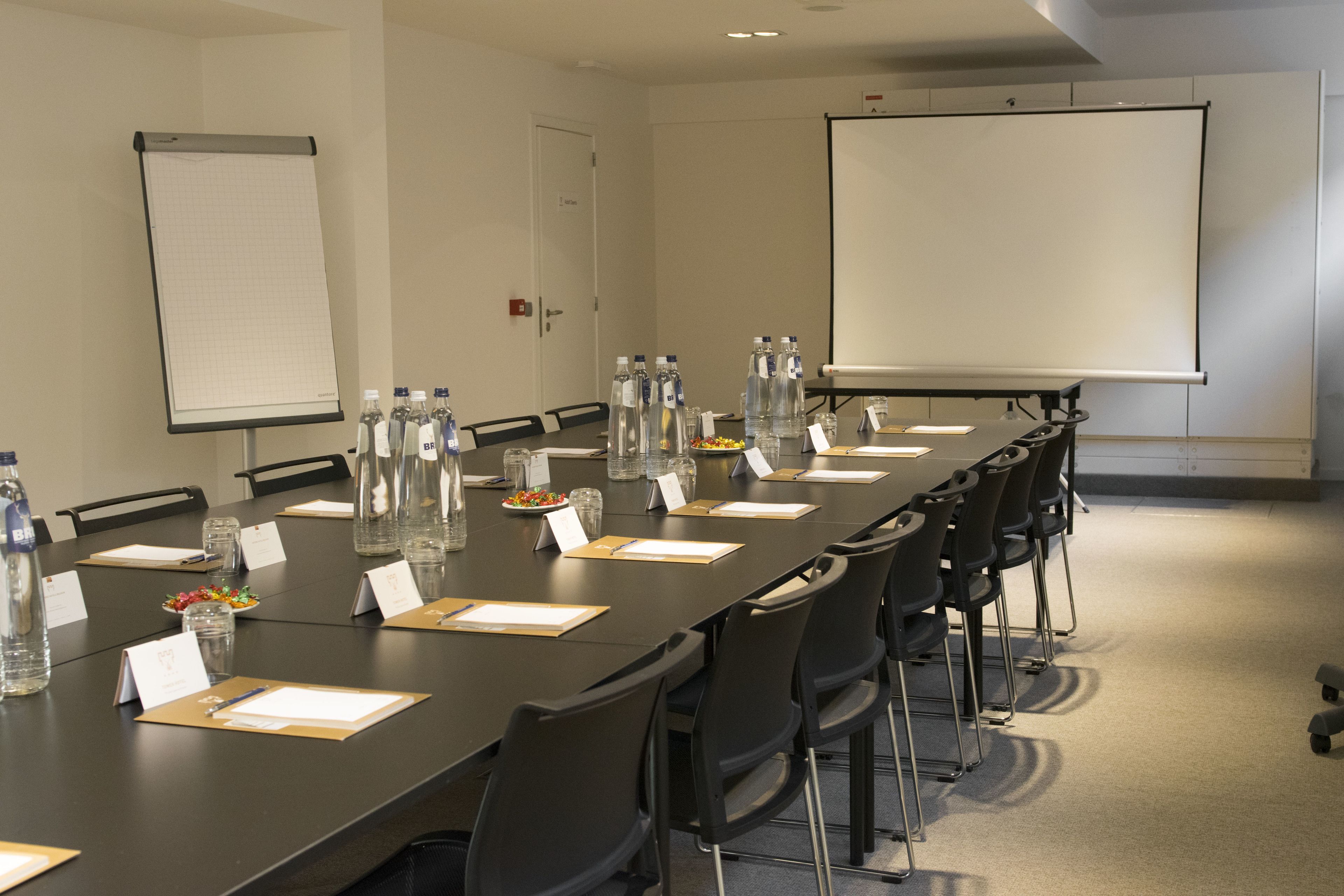 A conference room with a long table, chairs, a projector screen, and water bottles.