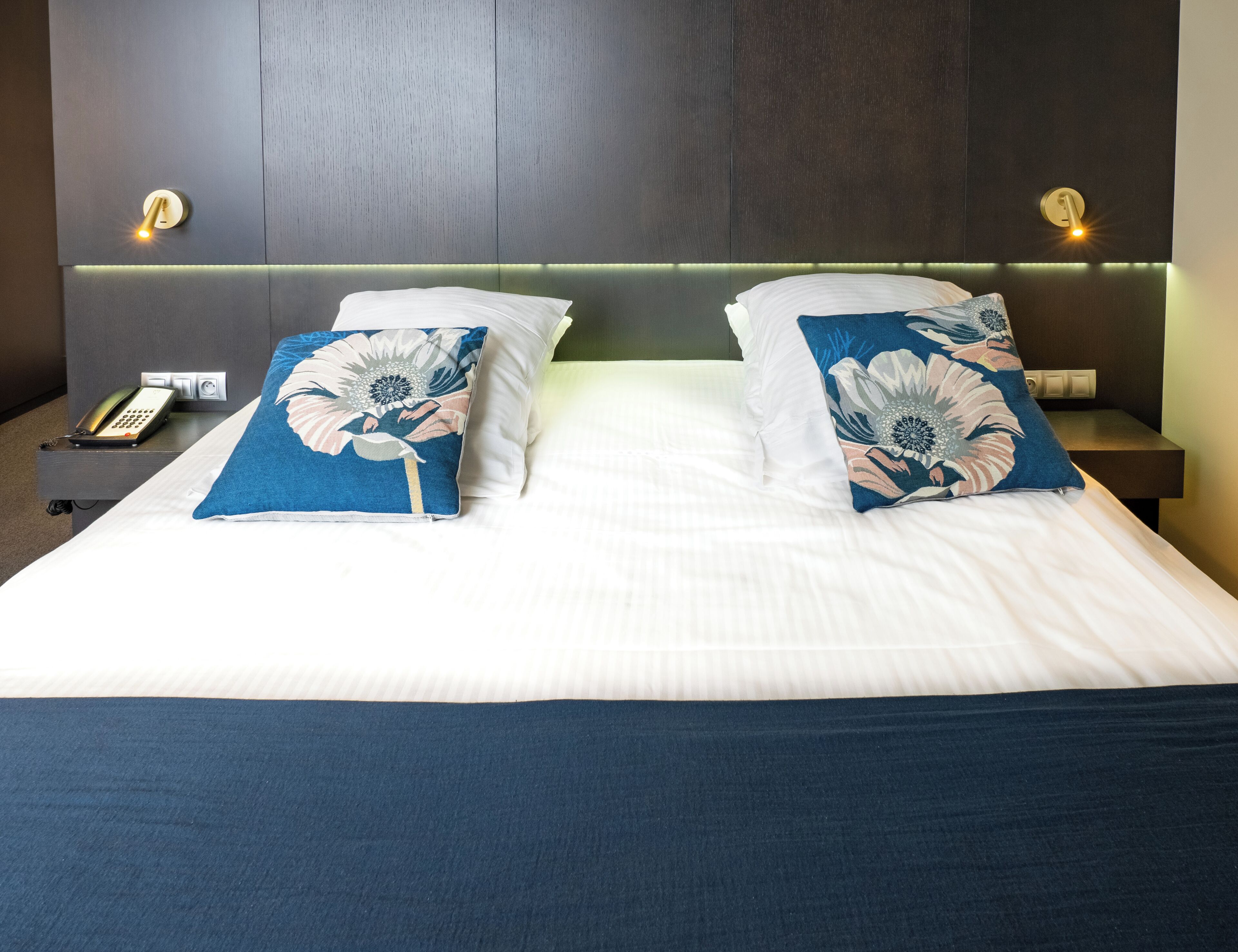 Habitación de hotel con una cama grande, dos mesitas de noche, un teléfono y lámparas fijadas a la pared.
