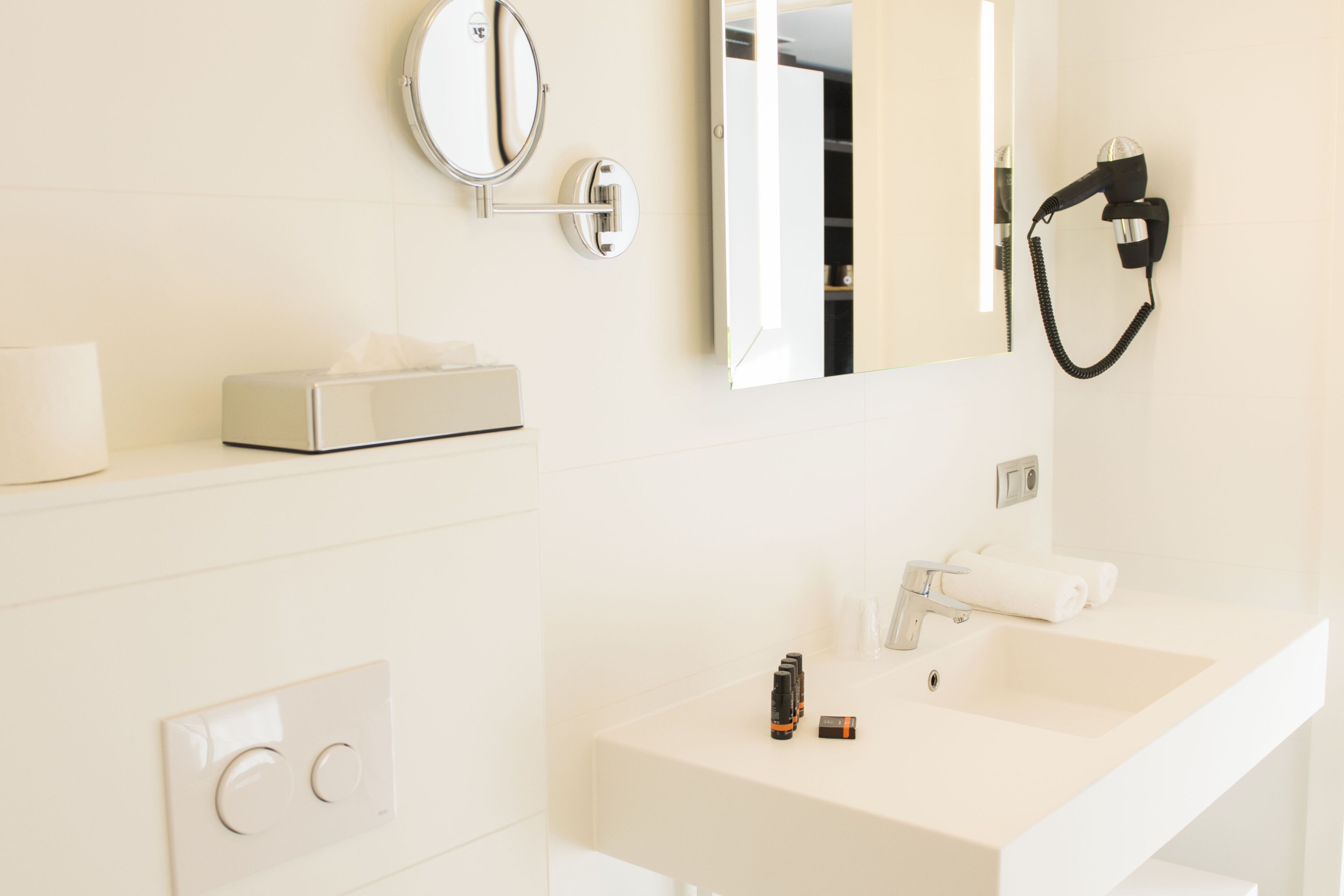 Ein modernes Badezimmer mit Waschbecken, Spiegel, Föhn und Handtuchhalter.