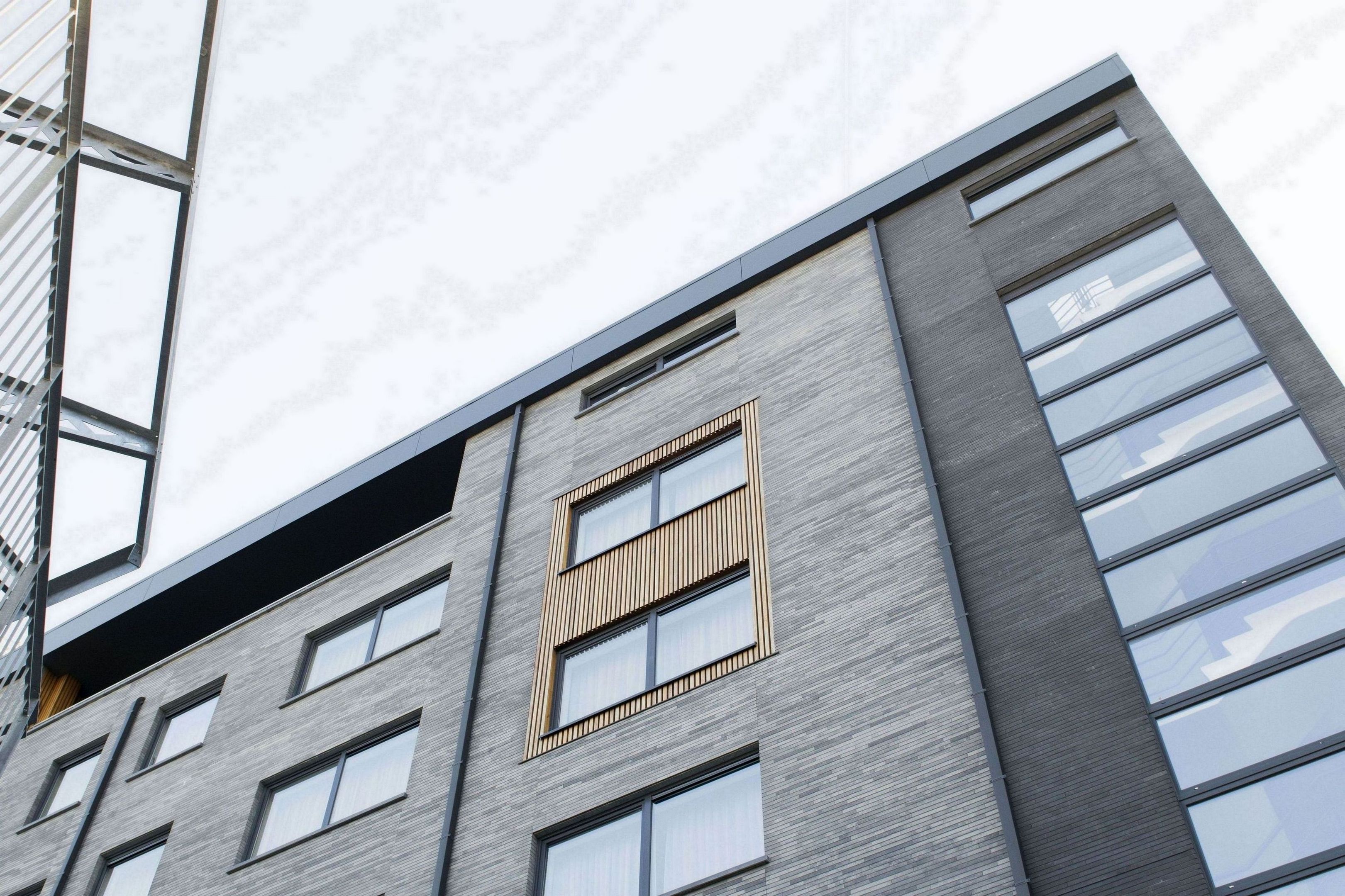 A modern building with a grey facade, large windows, and a unique window design with vertical slats.
