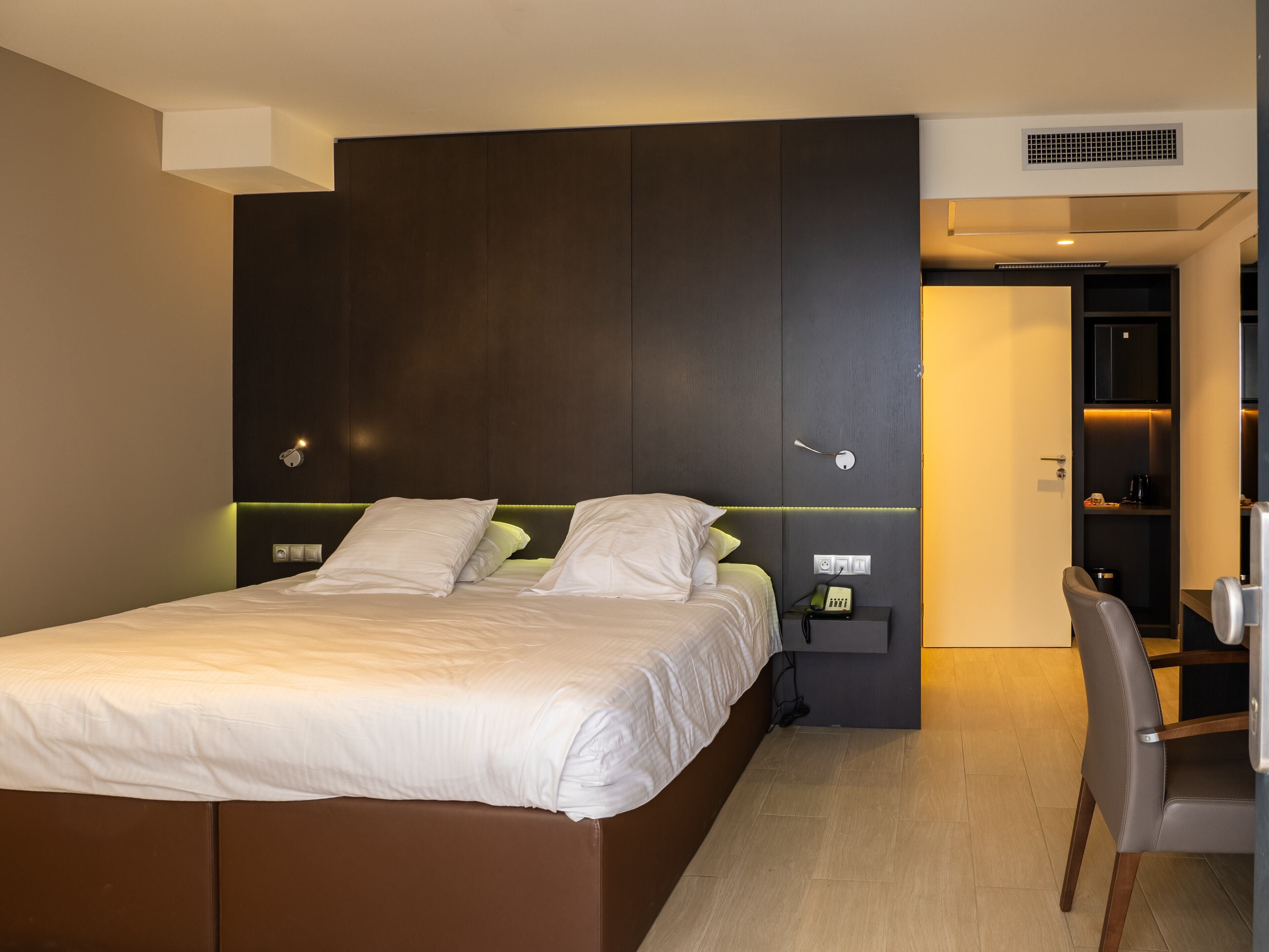 A modern hotel room with a large bed, bedside tables, a desk, and a chair.