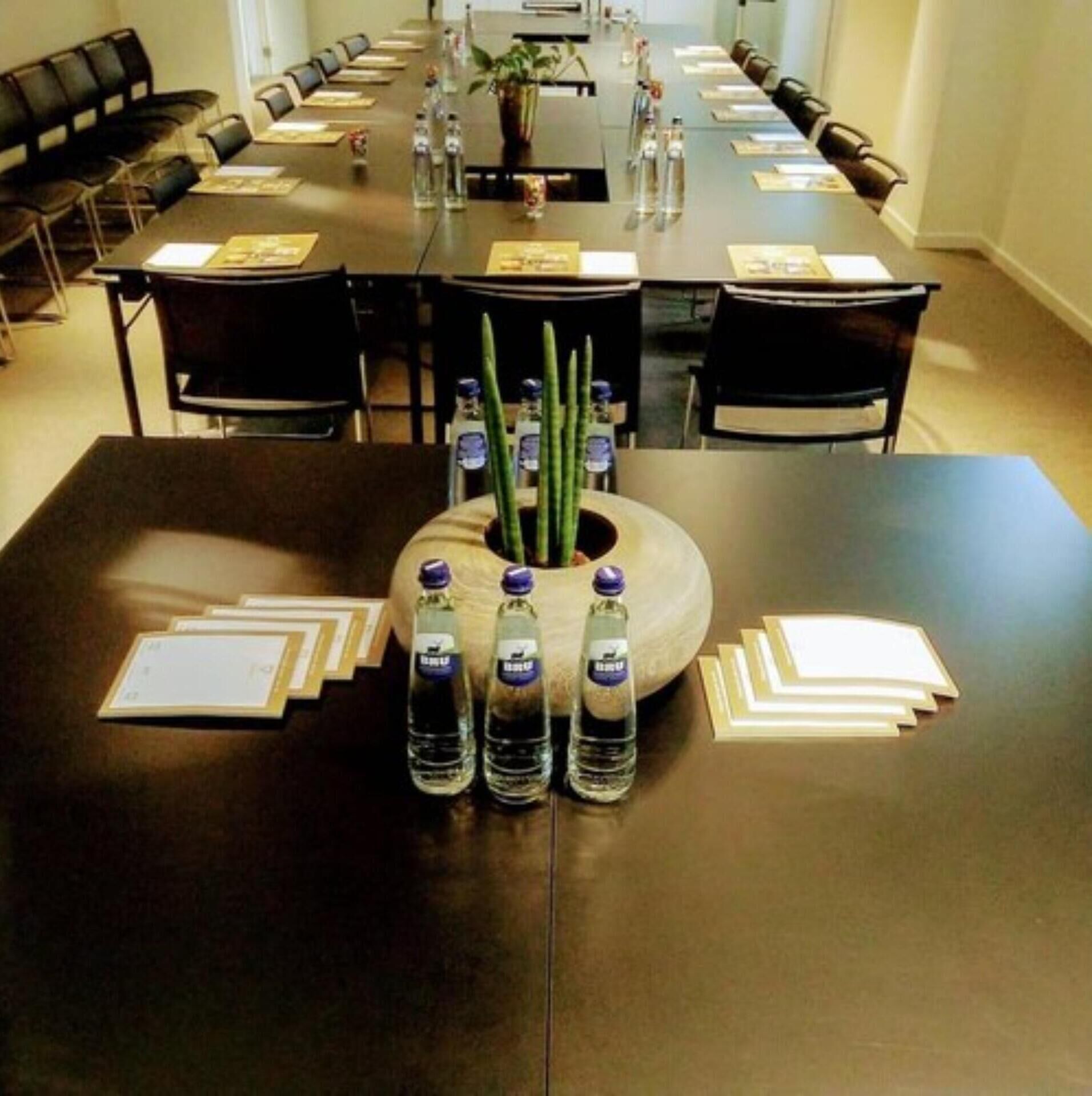 Une salle de conférence dotée d’une longue table préparée pour les réunions, avec des bouteilles d’eau et des porte-noms.
