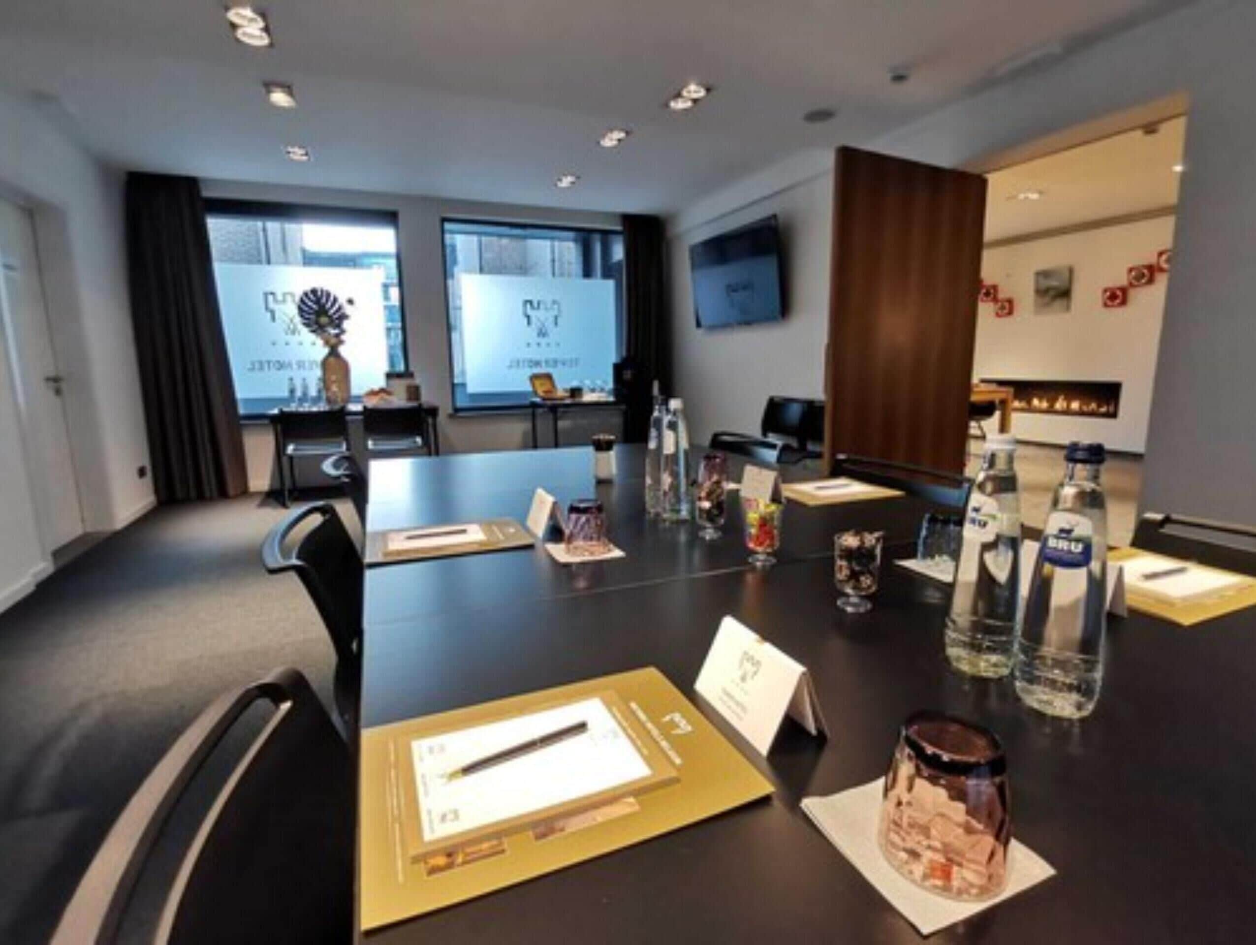 A conference room with a long table, chairs, and a projector screen.