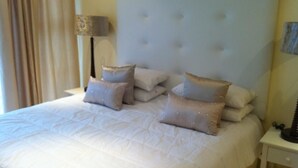 A neatly made bed with a tufted headboard, multiple pillows, and a bedside lamp. - Villa La Vida- Self-Catering House (Umhlanga)