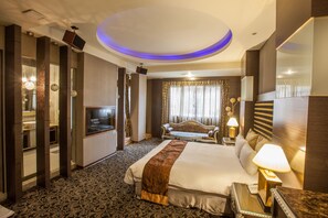 Una habitación de hotel con una cama grande, televisión, sofá y escritorio con lámpara.