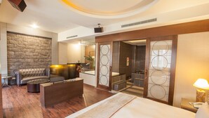 A modern hotel room with a large bed, a leather sofa, a small coffee table, a TV, and a bathroom with a glass door. - Spring Breeze Motel (Hualien City)